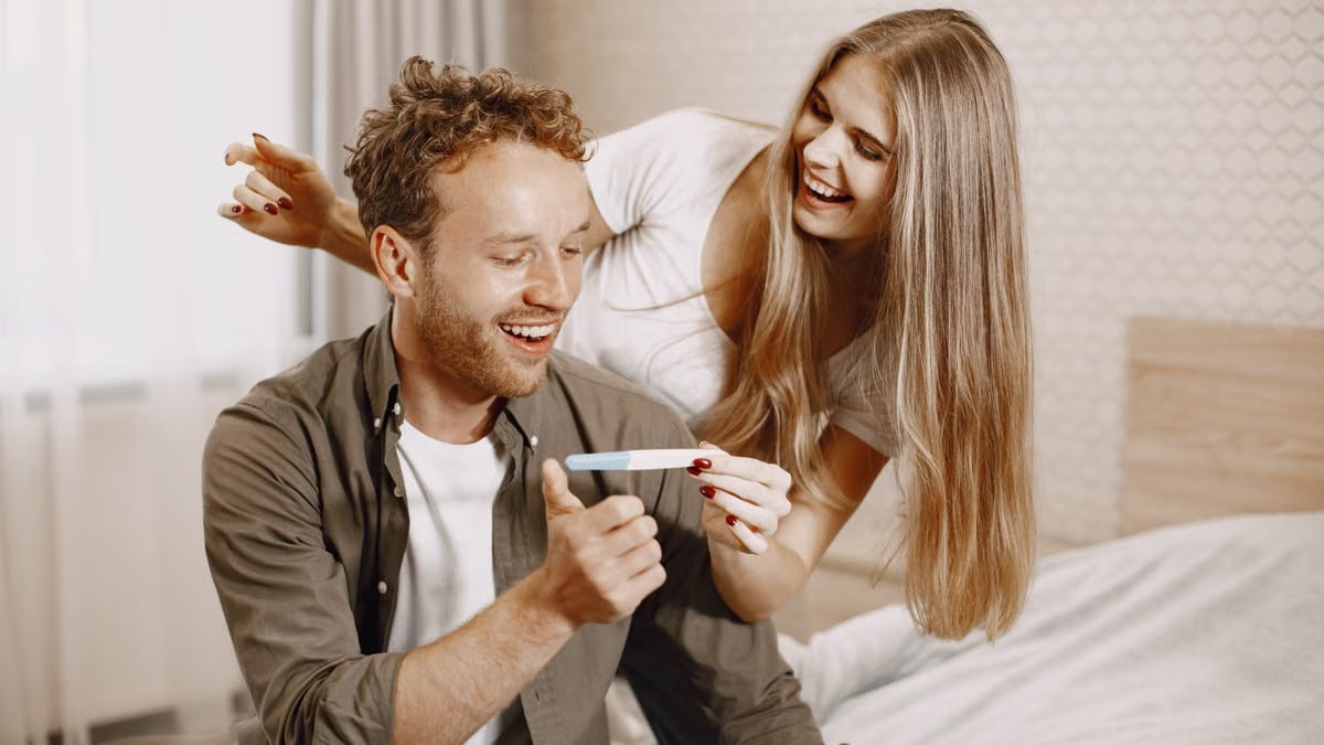 Happy couple indoors celebrating a positive pregnancy test result with smiles and joy.